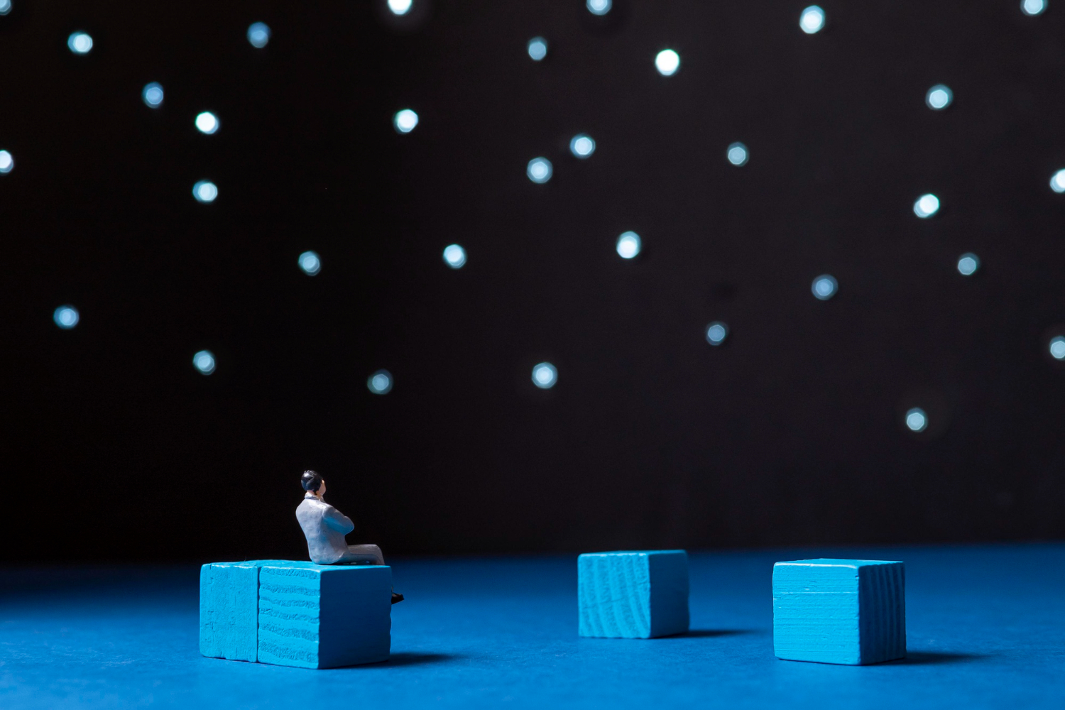 Miniature figure contemplating under a starry sky, symbolizing financial decision-making under uncertainty, with blue blocks representing potential strategies and outcomes in "What If" scenario planning.