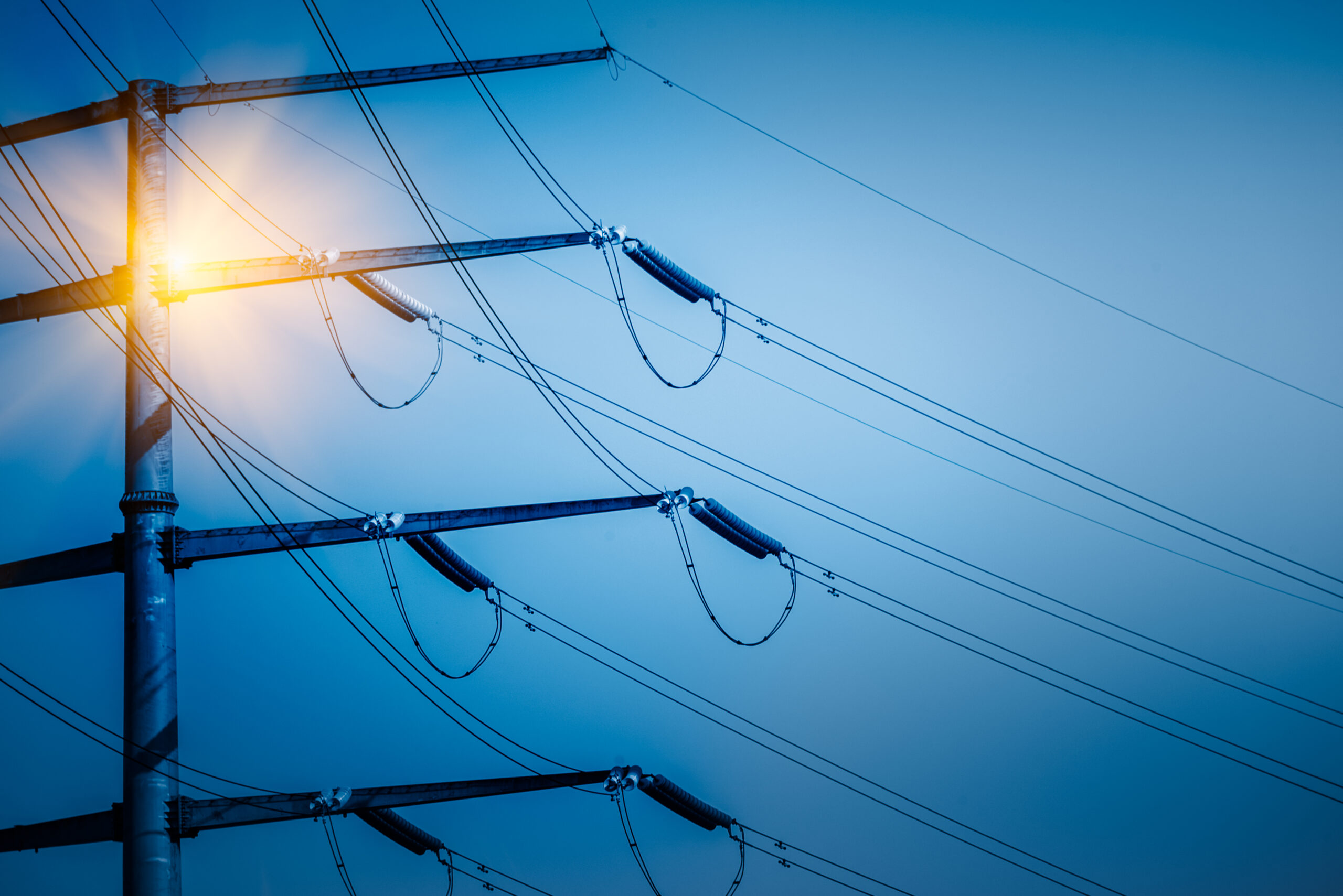 Poste de alta tensión con cables eléctricos iluminado, representando la infraestructura crítica de los servicios públicos, cuya eficiencia y seguridad pueden optimizarse mediante una gobernanza de datos efectiva.