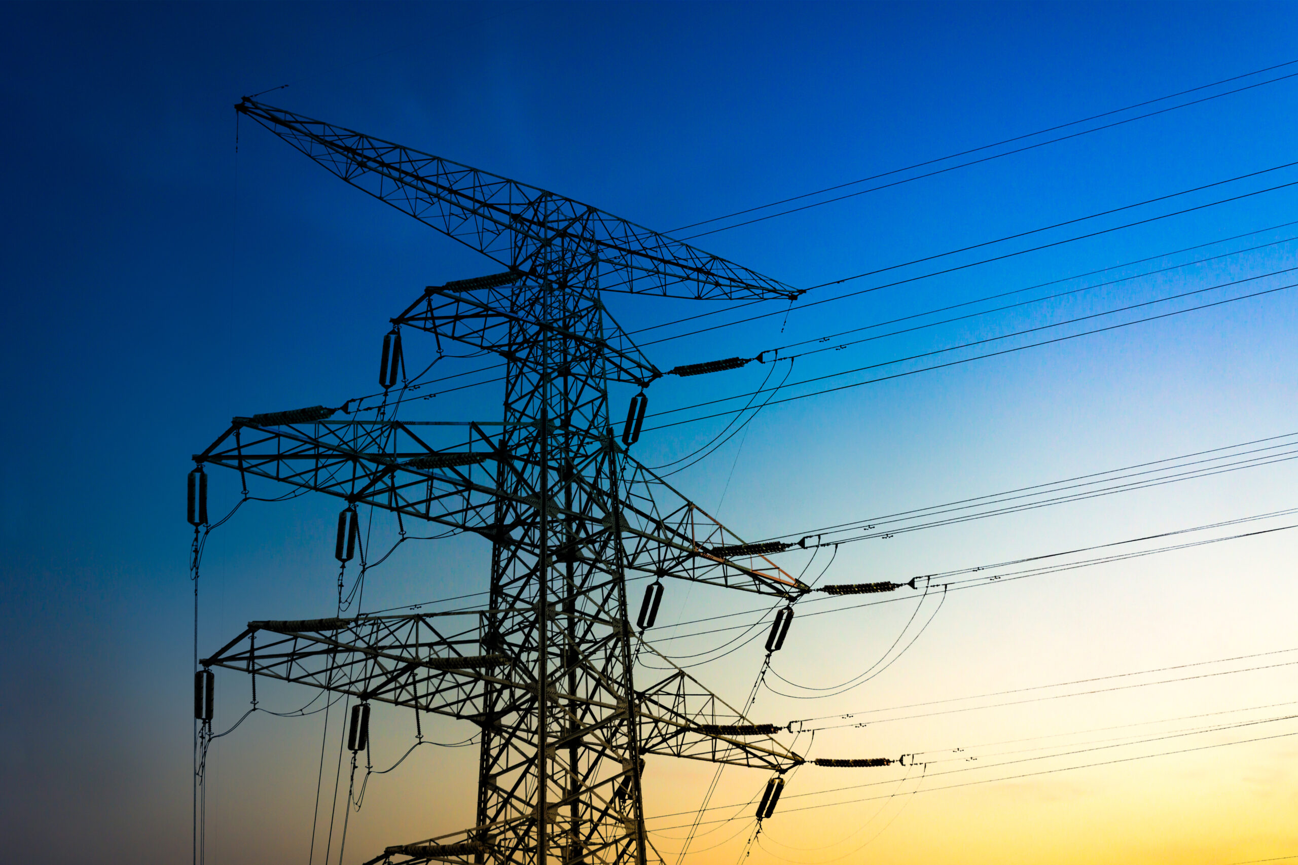 Torres de alta tensión al atardecer representando el sector de utilities, con cielo anaranjado y estructuras metálicas que simbolizan la infraestructura crítica donde se aplica la gobernanza de datos.