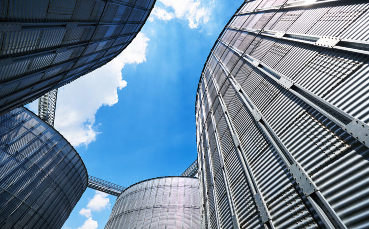 Upward view of modern metal silo structures against a bright blue sky, symbolizing digital transformation and infrastructure modernization in public water utilities.
