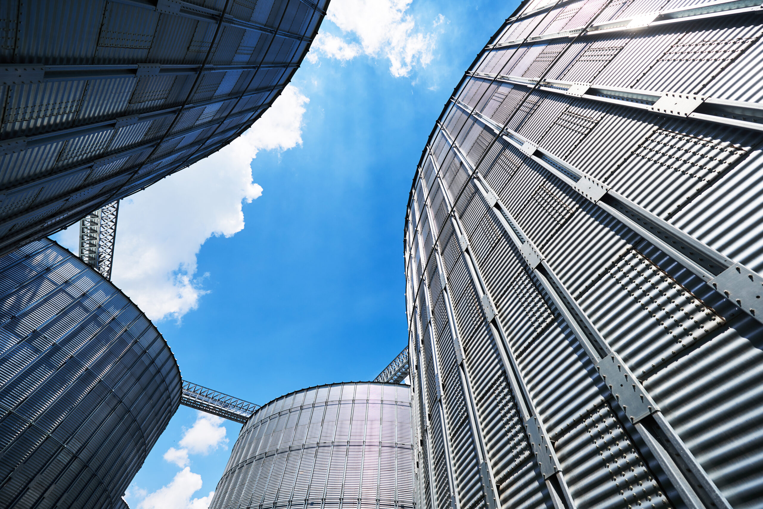 Upward view of modern metal silo structures against a bright blue sky, symbolizing digital transformation and infrastructure modernization in public water utilities.