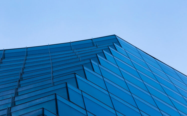Primer plano de la esquina superior de un rascacielos moderno con fachada de cristal azul, bajo un cielo claro. La imagen evoca la solidez y la visión de futuro, reflejando el concepto de un gobierno de datos robusto como cimiento para la inteligencia artificial y la predicción en el sector de servicios públicos.