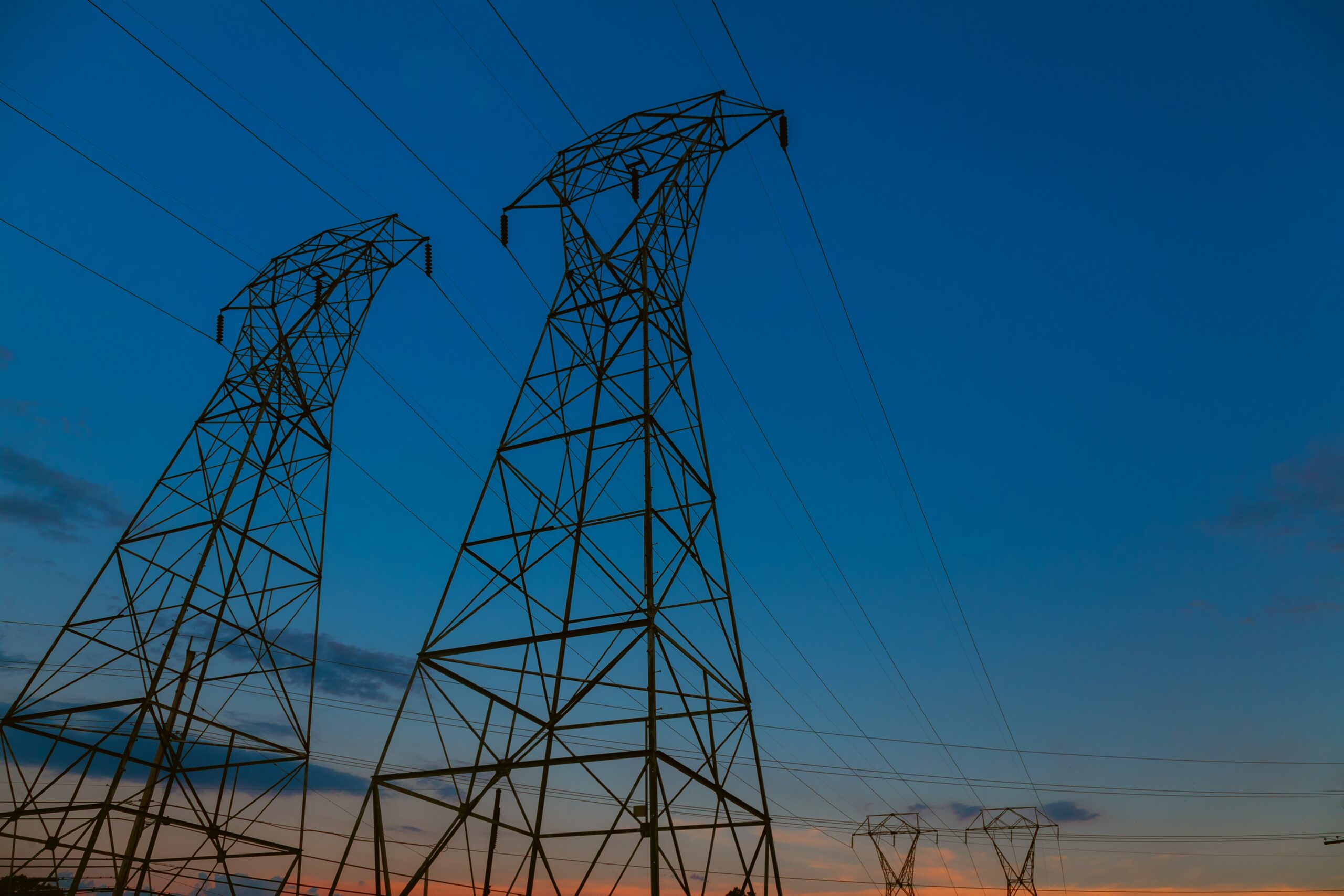 High-voltage transmission towers against a sunset sky, representing critical utility infrastructure and the need for operational resilience.